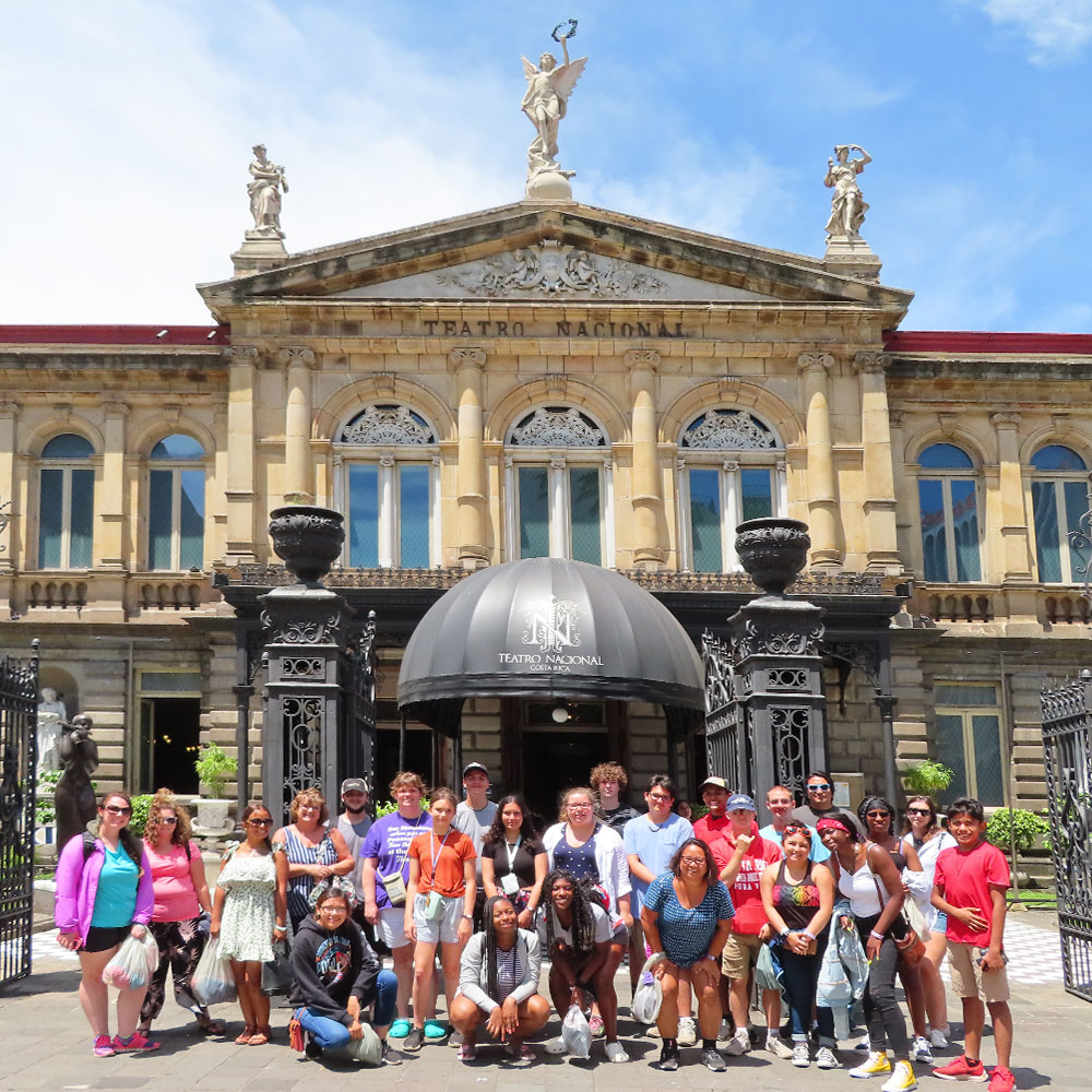 large class of students taking a group photo in front of a historical building in costa rica